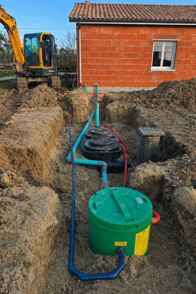 Assainissement : Installation d'une micro-station d'épuration Installation d'un système d'assainissement individuel avec micro-station et tuyaux devant une maison en briques.