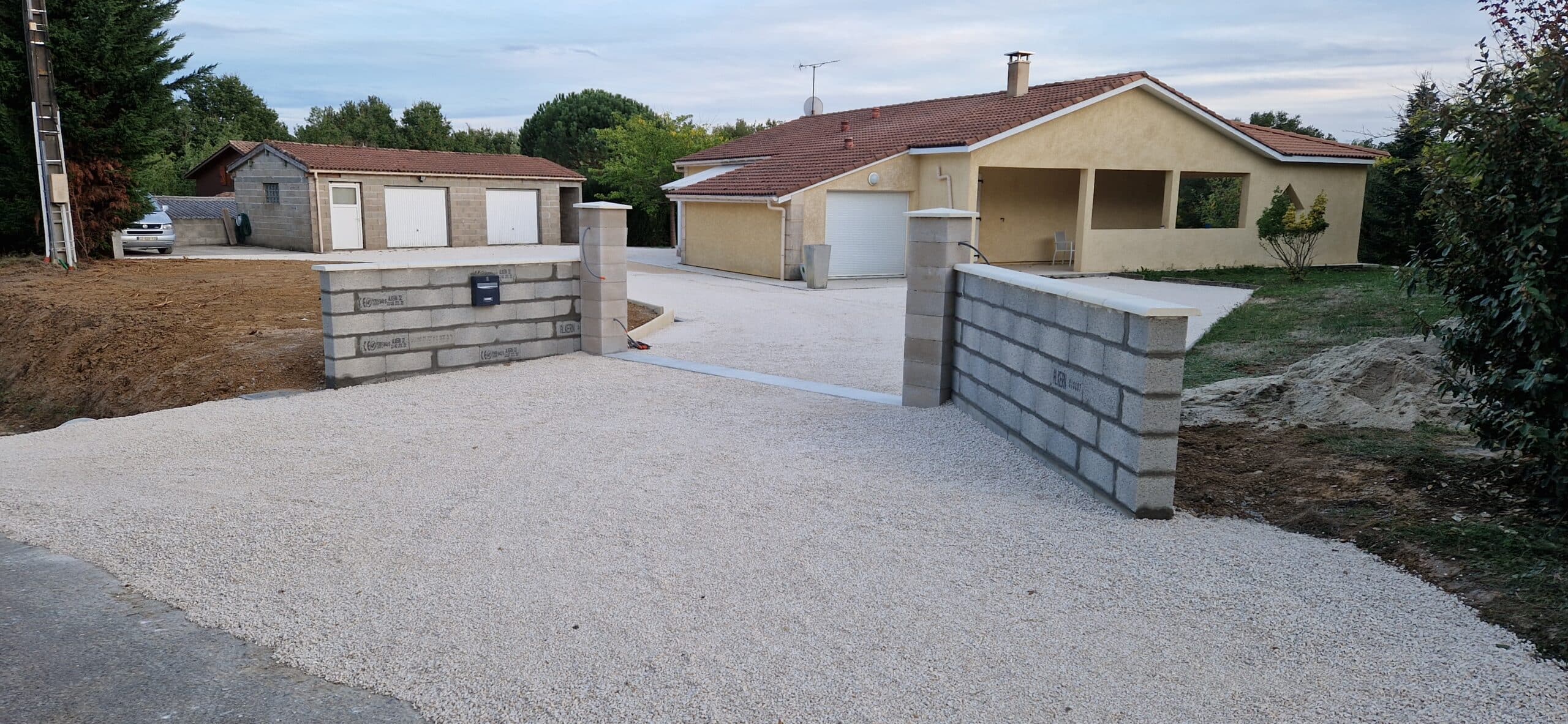 Entrée de maison avec allée en gravier blanc et murs de clôture en parpaings en cours de construction.