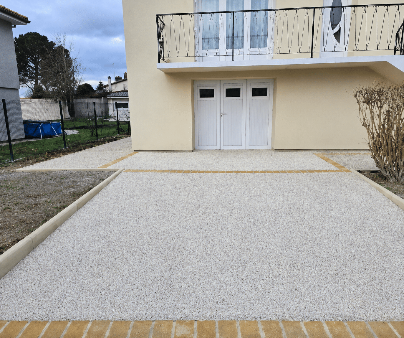 Aménagement d'une cour en moquette de pierre claire avec bordures en pavés jaunes devant une maison moderne.