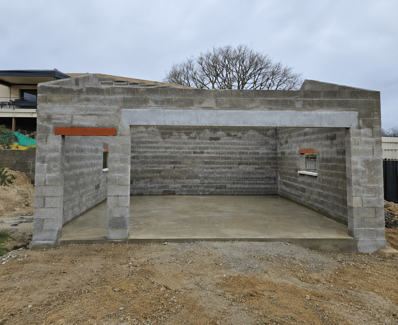 Construction d'un garage en blocs de béton avec sol lissé et linteaux apparents sur un terrain en terre.
