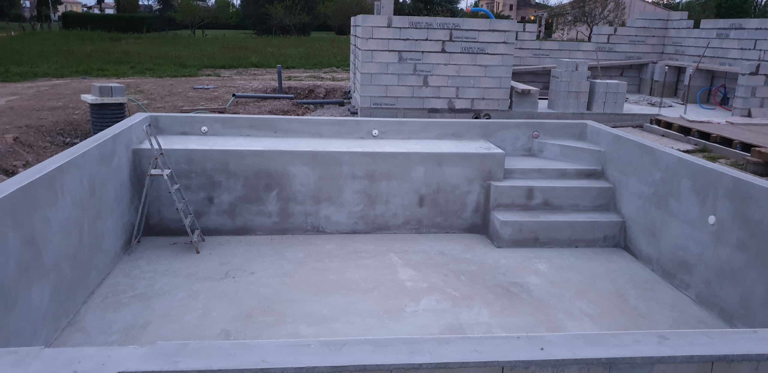 Piscine en béton en construction avec escalier intérieur, banquette et échelle métallique sur un chantier.