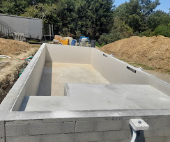Construction d'une piscine rectangulaire en béton avec escaliers intégrés sur un chantier de terrassement.