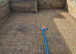 Treillis métallique et tuyau bleu au fond d'une excavation pour la construction d'une piscine ou de fondations.