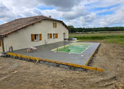Terrasse de piscine en béton frais avec coffrages devant une maison de campagne en rénovation.