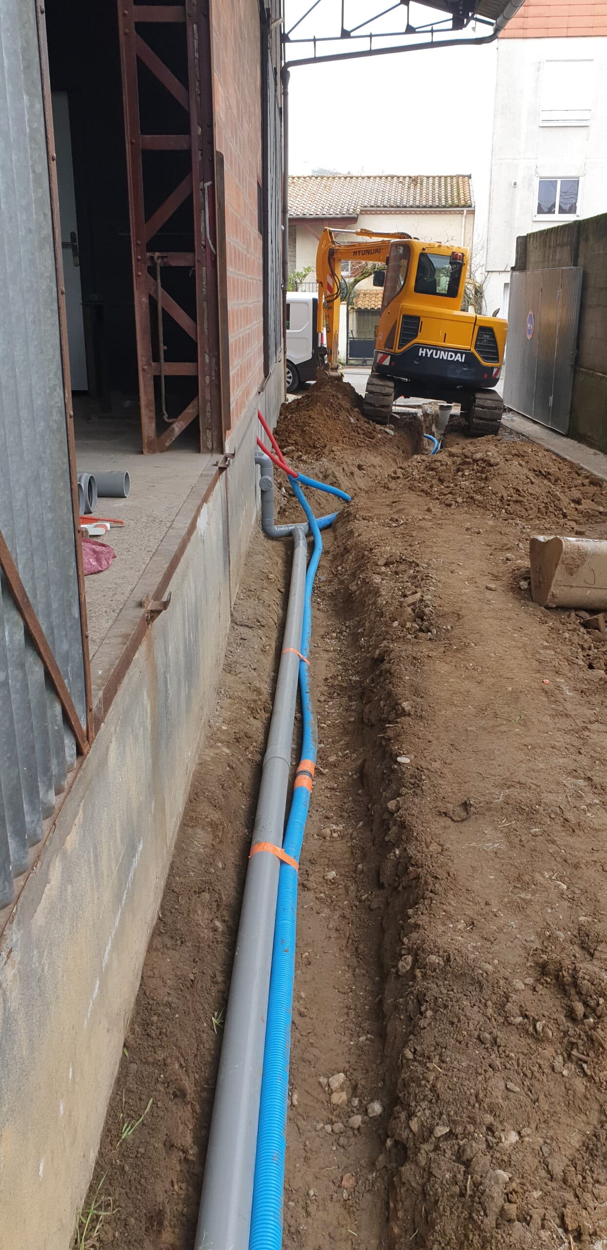 Mini-pelle Hyundai jaune et pose de tuyaux dans une tranchée de chantier de construction.