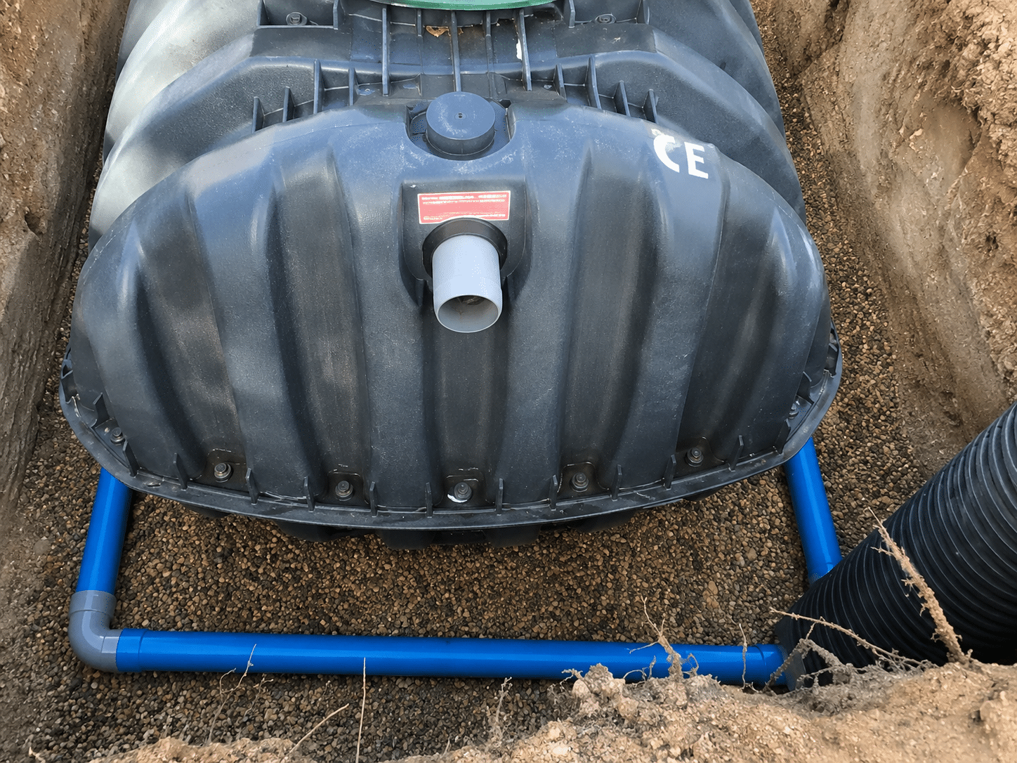 Cuve enterrée avec marquage CE et tuyaux bleus sur lit de gravier pour assainissement ou récupération d'eau.