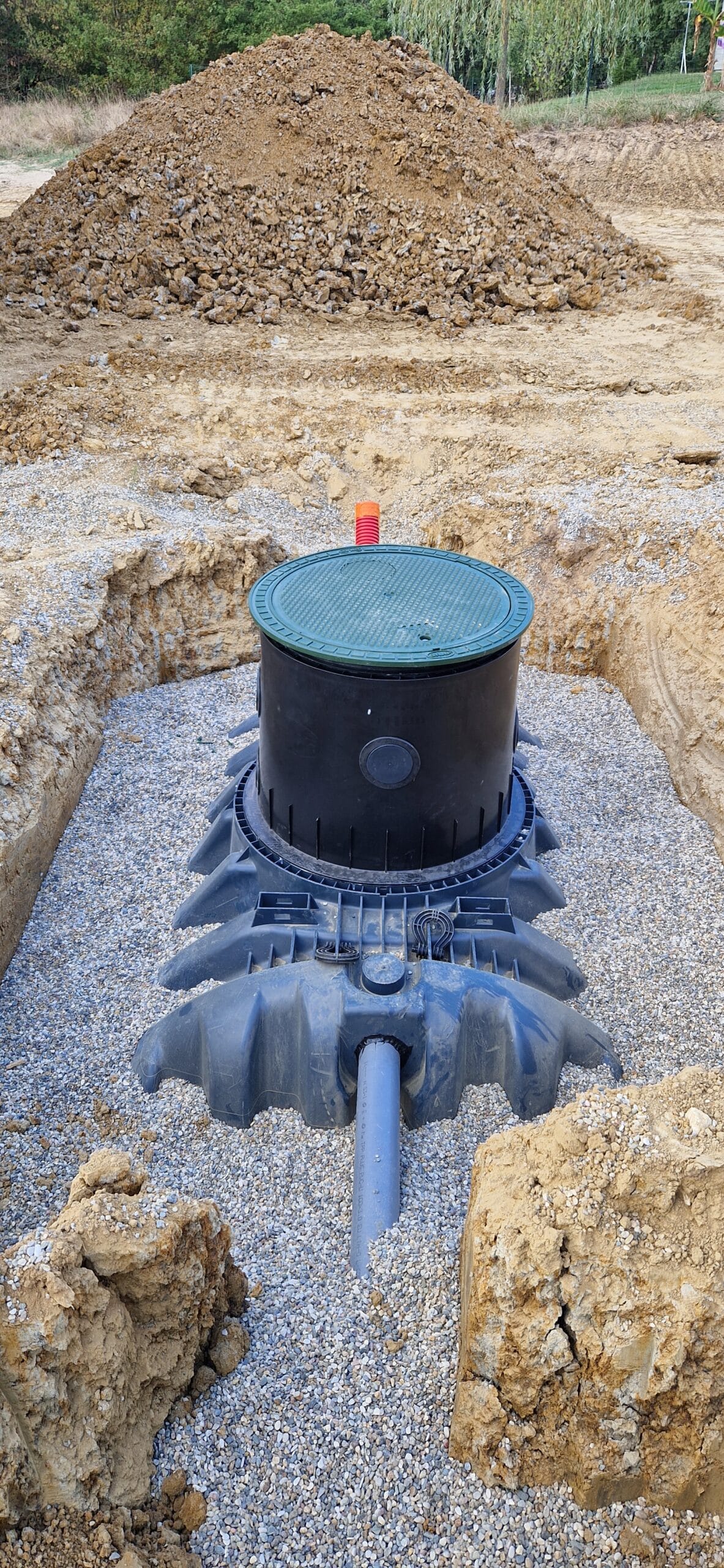 Installation d'une cuve de récupération d'eau de pluie enterrée dans une fosse avec graviers et tuyau d'évacuation.