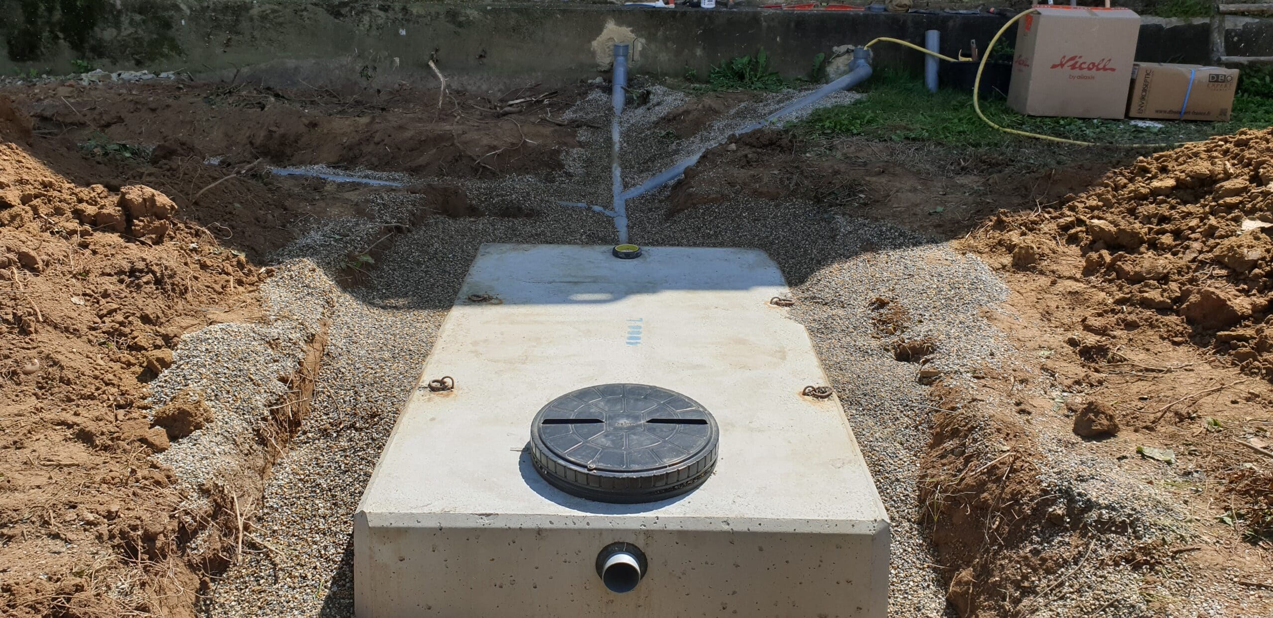 Installation d'une fosse septique en béton Nicoll dans une excavation avec tuyaux PVC et remblai de gravier.