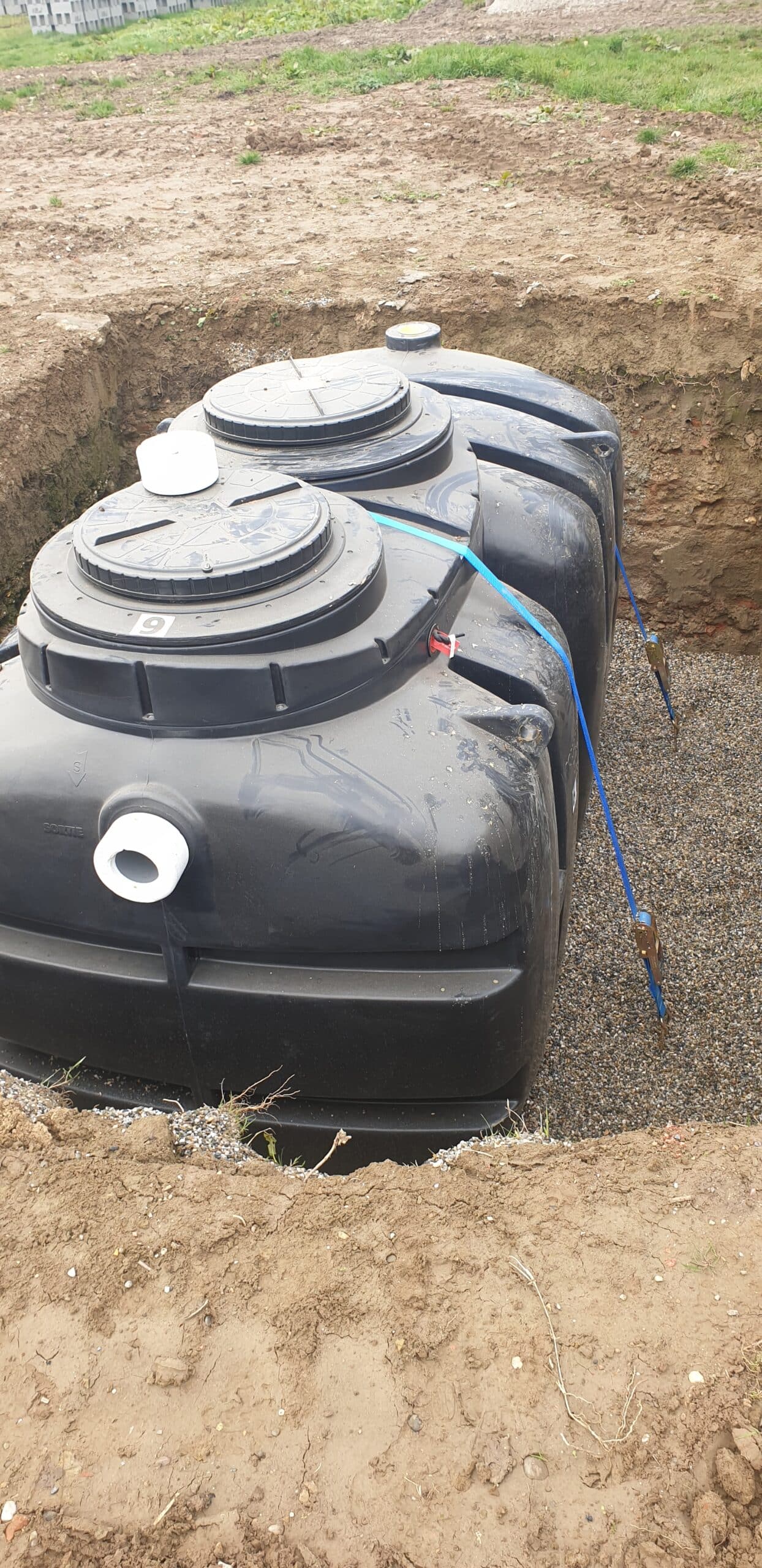 Fosse septique noire installée dans une excavation avec gravier. Inscriptions SORTIE et 9 visibles sur les couvercles.
