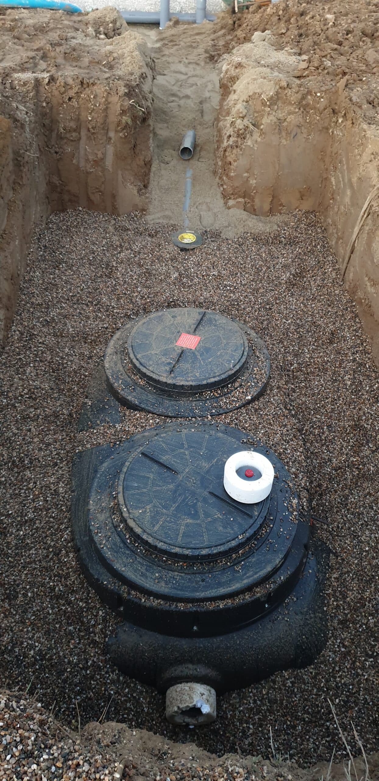 Installation d'une fosse septique en plastique noir dans une tranchée remplie de gravier avec deux couvercles.