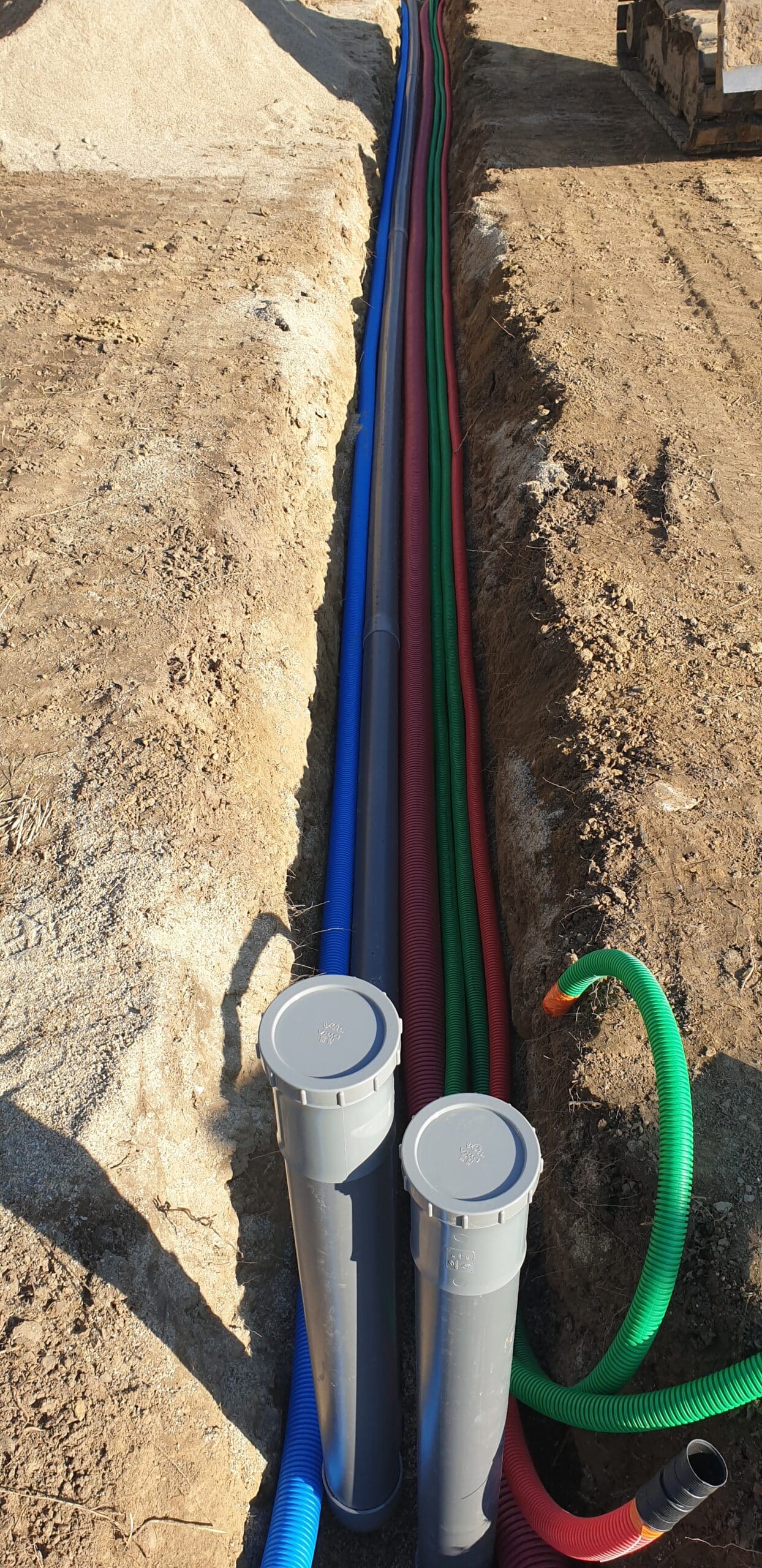 Gaines électriques et tuyaux de réseaux souterrains colorés installés dans une tranchée sur un chantier de construction.