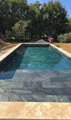 Piscine rectangulaire en carrelage gris foncé avec margelles en travertin clair et escalier immergé moderne.