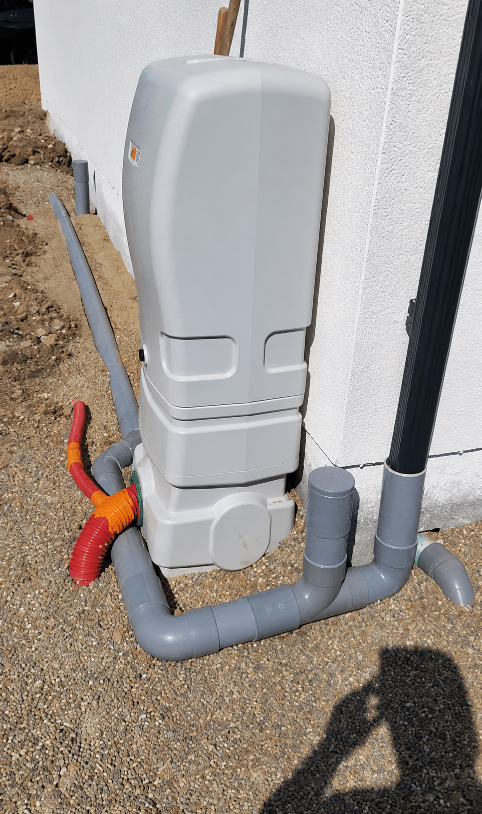 Installation extérieure d'une pompe à chaleur avec tuyaux PVC gris et gaines annelées orange sur gravier.