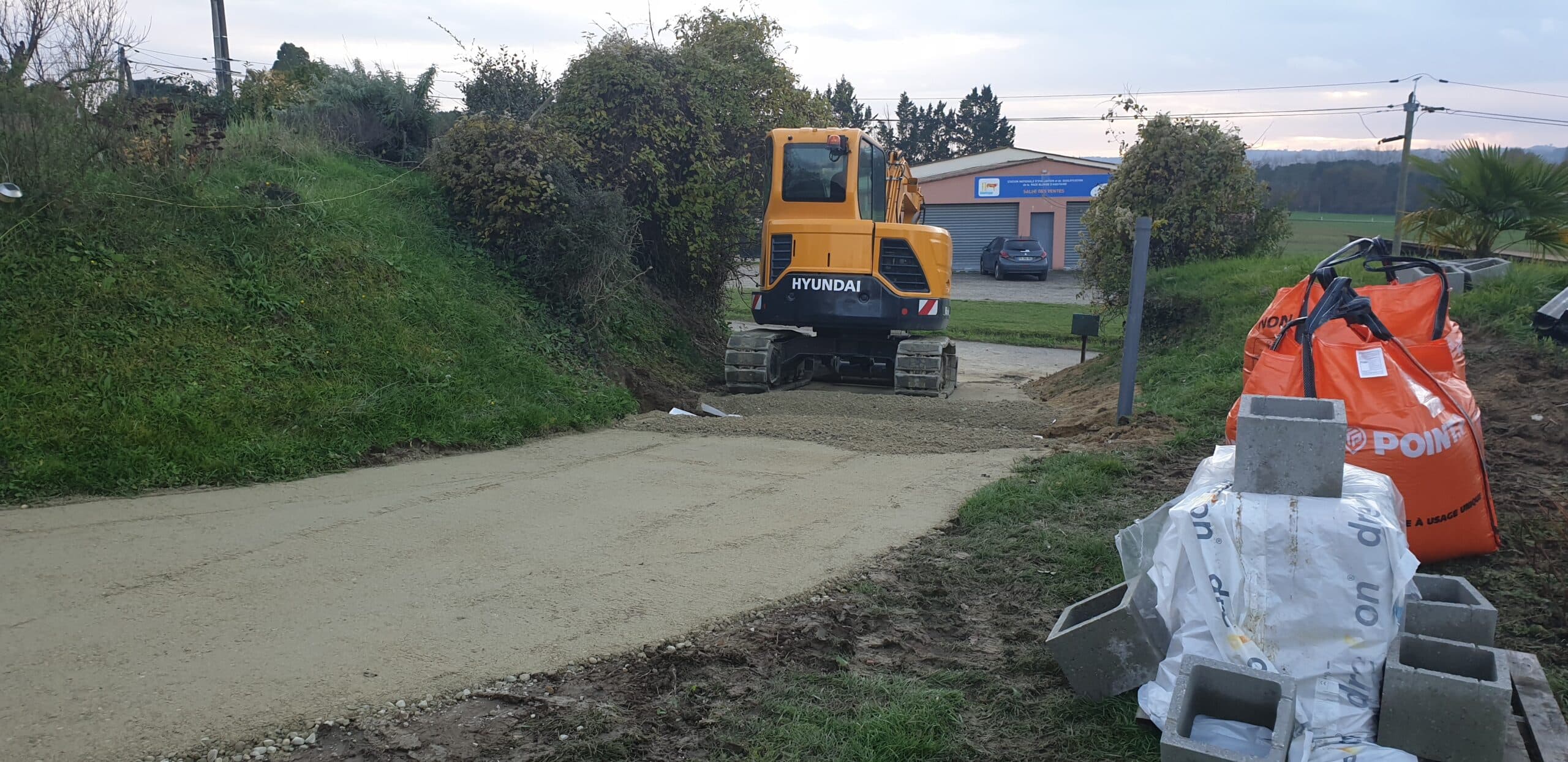 Excavatrice Hyundai jaune sur un chantier de terrassement avec sac Point.P et parpaings en bordure d'allée.